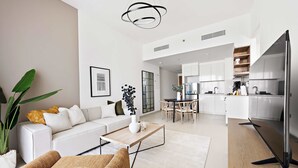 A modern living room with a sofa, coffee table, and a dining area with chairs. There is a kitchen with cabinets and a refrigerator. - Silkhaus Stylish 1BR Near Burj Khalifa Balcony (Dubai)