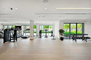 A modern gym with cardio machines, weight benches, and a large window providing natural light. - Silkhaus in Burj Royale Luxury 1bdr High Floor (Dubai)