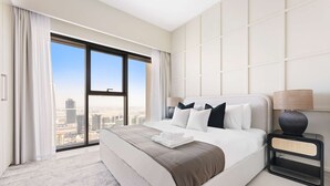 Ein modernes Hotelzimmer mit einem großen Bett, einem Nachttisch und Blick auf die Stadt durch raumhohe Fenster.