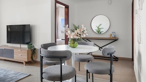 Una sala de estar moderna con televisor, sillones tapizados grises, una mesa redonda y un florero con flores.