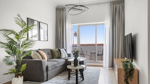 Una sala de estar moderna con un sofá gris, una mesa de centro, una planta en maceta y un televisor sobre un mueble de madera.
