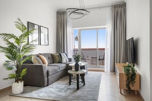 A modern living room with a grey sofa, a coffee table, a potted plant, and a TV on a wooden stand. - Silkhaus 1bdr in Art XII Easy Metro Access (Dubai)