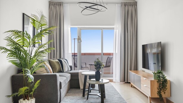 Una sala de estar moderna con un sofá gris, una mesa de centro, un televisor y un balcón con vistas.