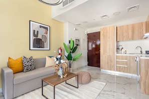 A modern living room with a sofa, coffee table, and a kitchen area with wooden cabinets and a sink. - Silkhaus Elite 1bdr Stay in Al Maryah Vista Tower (Abu Dhabi)