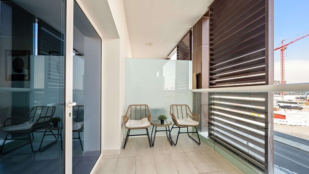 A balcony with two wicker chairs, a small table, and a view of a construction site. - Silkhaus Studio Masdar City Leonardo Residence (Abu Dhabi)