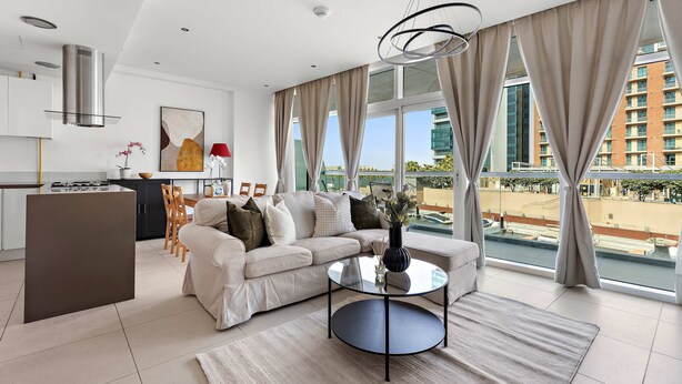 A modern living room with a sofa, coffee table, and a view of a cityscape through large windows. - Silkhaus Chic 1bdr in Al Bandar Al Naseem A (Abu Dhabi)