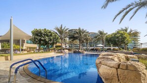 A swimming pool with a curved edge, surrounded by lounge chairs and palm trees. - Silkhaus Chic 1bdr in Al Bandar Al Naseem A (Abu Dhabi)