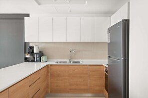 A modern kitchen with white cabinets, a stainless steel refrigerator, a sink, and wooden cabinetry. - Silkhaus Canal View 1BR Apartment In Reem Island (Abu Dhabi)