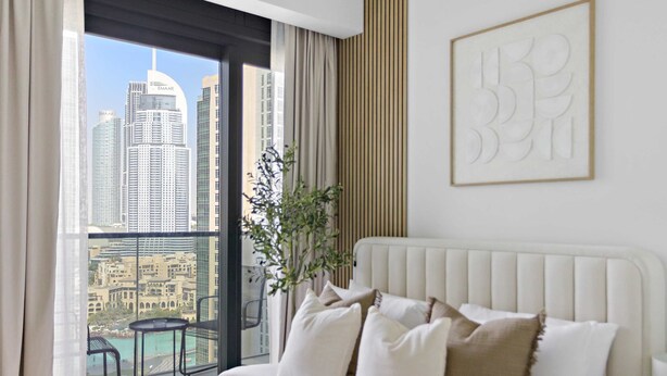 Habitació d'hotel amb una finestra gran que ofereix vistes a edificis alts, un llit amb roba de llit blanca i una obra d'art abstracta emmarcada a la paret.