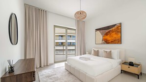 Un dormitorio moderno con una cama grande, una mesita de noche, una lámpara colgante, un ventanal con cortinas y vistas a un edificio.