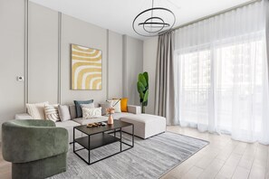 Ein modernes Wohnzimmer mit einer Eckcouch, einem grünen Sessel, einem Couchtisch und einem großen Fenster mit durchsichtigen Vorhängen.