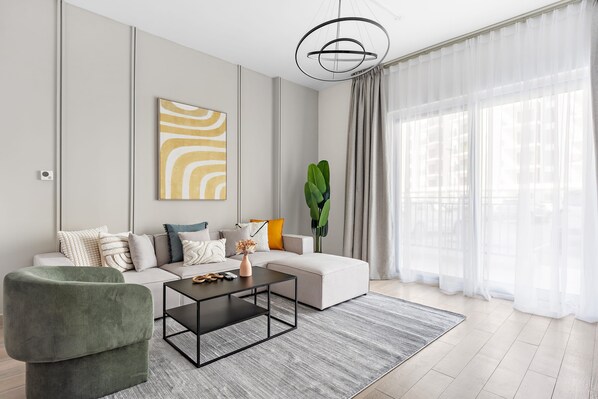 A modern living room with a sectional sofa, a green armchair, a coffee table, and a large window with sheer curtains. - 1BR Near Yas Marina w Building Pool hot tub (Abu Dhabi)