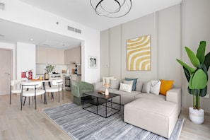 A modern living room with a sofa, coffee table, and chairs. There is a kitchen in the background. - 1BR Near Yas Marina w Building Pool hot tub (Abu Dhabi)