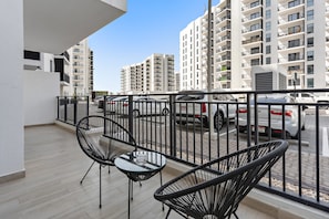 A balcony with two black wire-framed chairs and a small glass table, overlooking a parking area with several cars and tall residential buildings in the background. - 1BR Near Yas Marina w Building Pool hot tub (Abu Dhabi)
