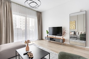 A modern living room with a sofa, coffee table, TV, and a large mirror. - 1BR Near Yas Marina w Building Pool hot tub (Abu Dhabi)