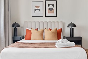 A neatly made bed with a white and brown bedspread, two black nightstands with lamps, and two framed abstract artworks on the wall. - Silkhaus Near Metro Art XII Tower Pool Gym (Dubai)
