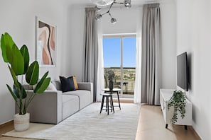Ett modernt vardagsrum med en soffa, ett soffbord, en tv och en balkong med gardiner.