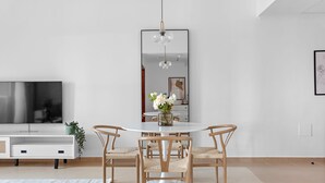 Een moderne eetruimte met een ronde tafel, vier stoelen, een centrale vaas met bloemen, een hanglamp en een grote spiegel aan de muur.