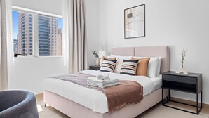 Een moderne slaapkamer met een groot bed, een nachtkastje, een stoel en een raam met gordijnen.
