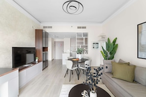 A modern living room with a dining area, a sofa, and a TV. - Silkhaus Canalside 1BR Water s Edge Yas Island (Abu Dhabi)