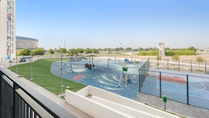 A playground with various play equipment, a basketball court, and a building with a mural in the background. - Silkhaus in Water s Edge Close to Ferrari World (Abu Dhabi)