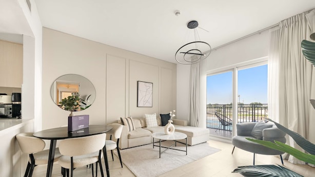 A modern living room with a sofa, coffee table, and dining area. There is a large window with a view of the outdoors. - Silkhaus in Water s Edge Close to Ferrari World (Abu Dhabi)