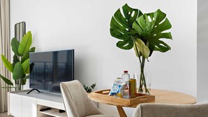 A modern living room with a flat-screen TV, two beige chairs, a wooden coffee table with snacks and drinks, and a large green plant. - Silkhaus Canal View Studio Near Ferrari World (Abu Dhabi)