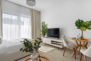 Una habitación de hotel moderna con sofá, televisión, mesa de comedor con sillas y plantas en macetas.