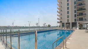 A swimming pool with a metal fence, surrounded by a tiled deck and a high-rise building with balconies. - Silkhaus Canal View Studio Near Ferrari World (Abu Dhabi)