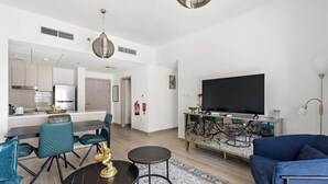 Ein modernes Wohnzimmer mit großem Fernseher, blauem Sofa und einem Essbereich mit türkisfarbenen Stühlen.