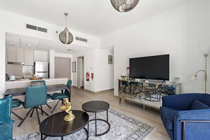 Ein modernes Wohnzimmer mit großem Fernseher, blauem Sofa und einem Essbereich mit türkisfarbenen Stühlen.