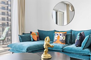 Un canapé de couleur bleu-vert avec des coussins colorés, une statue dorée et un miroir rond posé sur une table sombre.