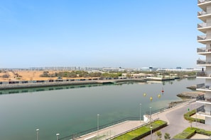 A waterfront view with a clear sky, a calm river, and a modern building with balconies. - Silkhaus Canalside Studio in Water s Edge Tower (Abu Dhabi)