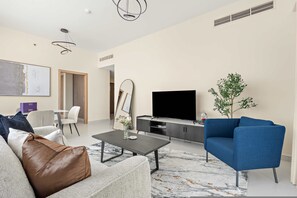 Ett modernt vardagsrum med en soffa, ett soffbord, en blå fåtölj, en platt-TV och en växt.