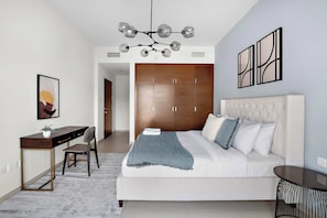 A modern bedroom with a large bed, a desk, and a chair. There is a wardrobe with multiple doors and a ceiling light fixture. - Silkhaus Urban 1BR Stay ARC Tower in Reem Island (Abu Dhabi)
