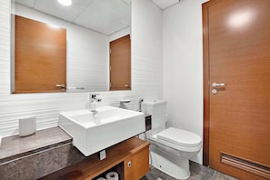 A modern bathroom with a white sink, wooden vanity, a toilet, and a wooden door. - Silkhaus Urban 1BR Stay ARC Tower in Reem Island (Abu Dhabi)