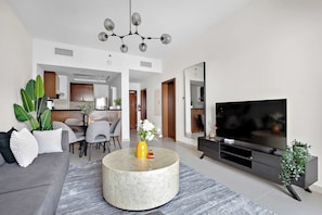 Un salon moderne avec un canapé gris, une table basse ronde, un téléviseur à écran plat et, au fond, un coin repas.