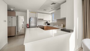 A modern kitchen with white cabinetry, a central island, and a stainless steel refrigerator. - Silkhaus 2BR Maid Room in Reem Island Radiant (Abu Dhabi)