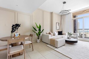 En moderne stue med spiseplads, en hvid sofa, et sofabord og et stort vindue med byudsigt.