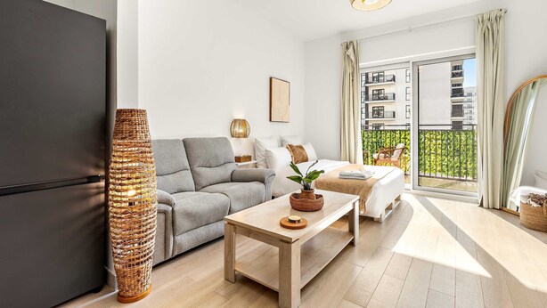 A modern living room with a sofa, a coffee table, a wicker lamp, and a large window with a balcony view. - Silkhaus Chic Studio Yas Island Near Sea World (Abu Dhabi)