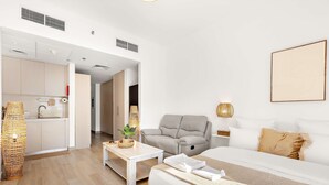 A modern hotel room with a bed, a grey armchair, a small table, and a kitchenette in the background. - Silkhaus Chic Studio Yas Island Near Sea World (Abu Dhabi)