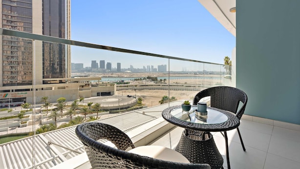 A balcony with a glass table and chairs, overlooking a cityscape with tall buildings and a body of water. - Silkhaus Premium 1BR at Amaya Tower in Reem Island (Abu Dhabi)