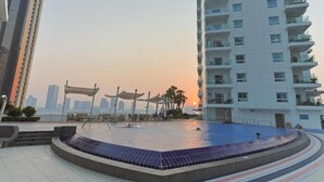 A swimming pool area with a sunken design, surrounded by a modern building with balconies. - Silkhaus Premium 1BR at Amaya Tower in Reem Island (Abu Dhabi)