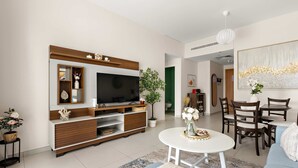 A modern living room with a flat-screen TV, wooden entertainment unit, dining table, and chairs. - Silkhaus Premium 1BR at Amaya Tower in Reem Island (Abu Dhabi)