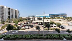 A parking lot with multiple cars, a building with a curved facade, and a tall residential building in the background. - Silkhaus Unique Deal Modern 2bdr Canal View (Abu Dhabi)