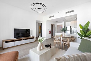 Ein modernes Wohnzimmer mit Flachbildfernseher, Couchtisch mit Vase und Essbereich mit Tisch und Stühlen.