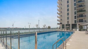 A swimming pool with a tiled deck, surrounded by a fence, and adjacent to a multi-story building with balconies. - Silkhaus Unique Deal Modern 2bdr Canal View (Abu Dhabi)