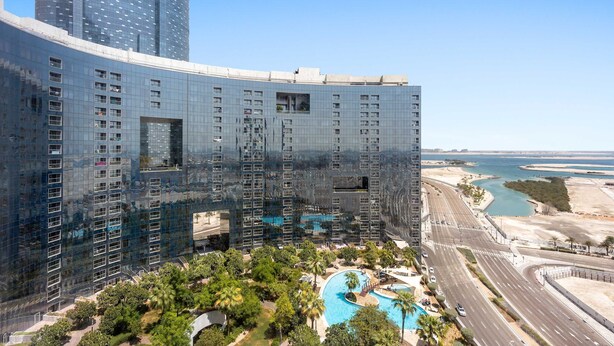 A modern hotel with a curved glass facade, a swimming pool, and a view of the coastline. - Silkhaus Modern Studio Arc Tower Reem Island (Abu Dhabi)