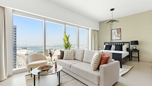 A modern hotel room with a large window offering a city view, a sofa, a small round table, and a bed with a nightstand. - Silkhaus Modern Studio Arc Tower Reem Island (Abu Dhabi)