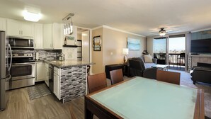 A modern kitchen with stainless steel appliances, a dining area with a glass-top table, and a living space with a TV and seating. - Harbor & Ocean View Coastal Retreat – Walk to Beach & Marina (Oceanside)